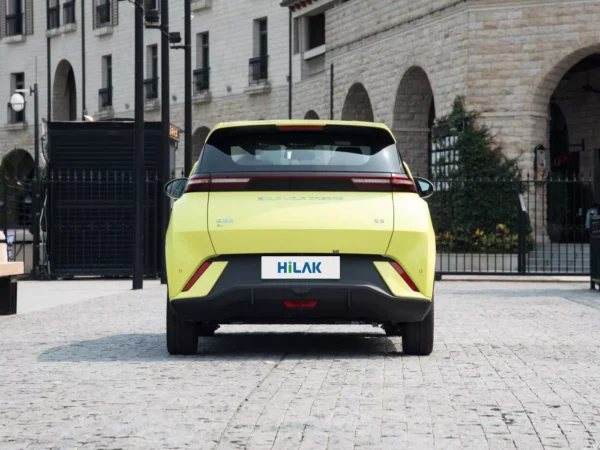 Detail view of the rear of a yellow BYD Seagull electric car, with the shadow of the vehicle falling on the brick road to the left.