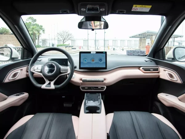 A detailed view of the cab of a white BYD Seagull electric car with a screen on the right side of the steering wheel and pink and black interior colors.