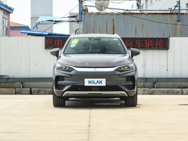 Front view of a gray BYD Tang electric car with the vehicle parked on a concrete pavement with a tin wall in the background.