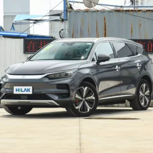 A left front view of a gray BYD Tang electric car with the vehicle parked on a concrete pavement with a tin wall in the background.