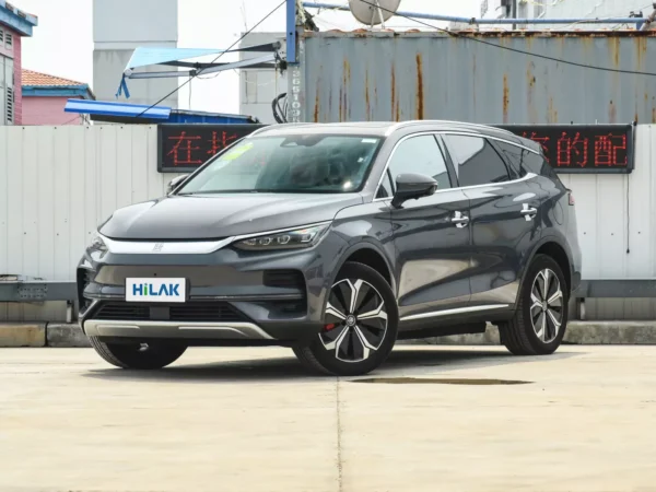 A left front view of a gray BYD Tang electric car with the vehicle parked on a concrete pavement with a tin wall in the background.