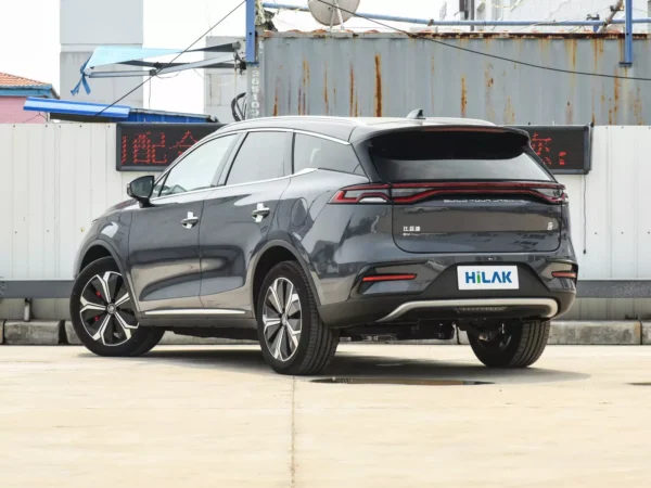 Left rear view of a gray BYD Tang electric car with the vehicle parked on a concrete pavement with a tin wall in the background.