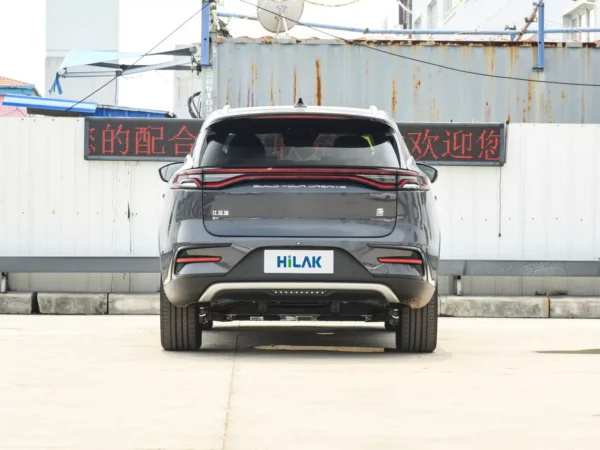 Rear view of a gray BYD Tang electric car with the vehicle parked on a concrete pavement with a tin wall in the background.