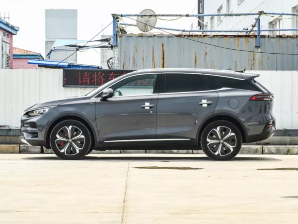 Side view of a gray BYD Tang electric car with a tin wall in the background.