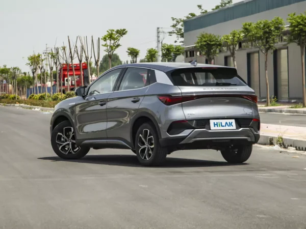 Close-up picture of the side and rear of a silver gray BYD Yuan Plus electric car parked on a tarmac road with trees lining the road.