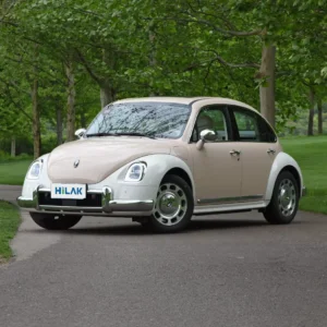 Left front view of a cream and white matching Ora Ballet Cat electric car parked on an asphalt surface flanked by many trees.