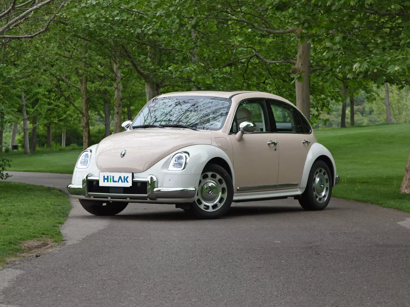 Left front view of a cream and white matching Ora Ballet Cat electric car parked on an asphalt surface flanked by many trees.