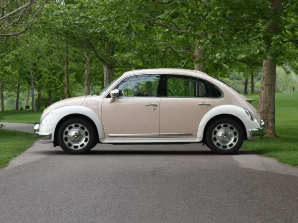 Side view of a cream and white matching Ora Ballet Cat electric car with lots of green foliage on the books on both sides of the road.