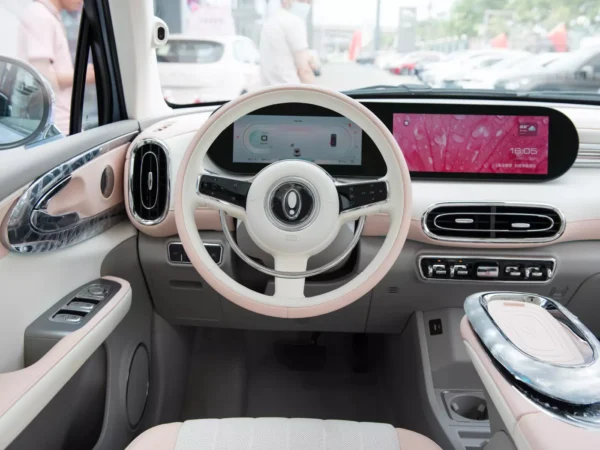 A detailed image of the steering wheel inside an Ora Ballet Cat electric car, consisting of two colors, pink and white, next to two screens.