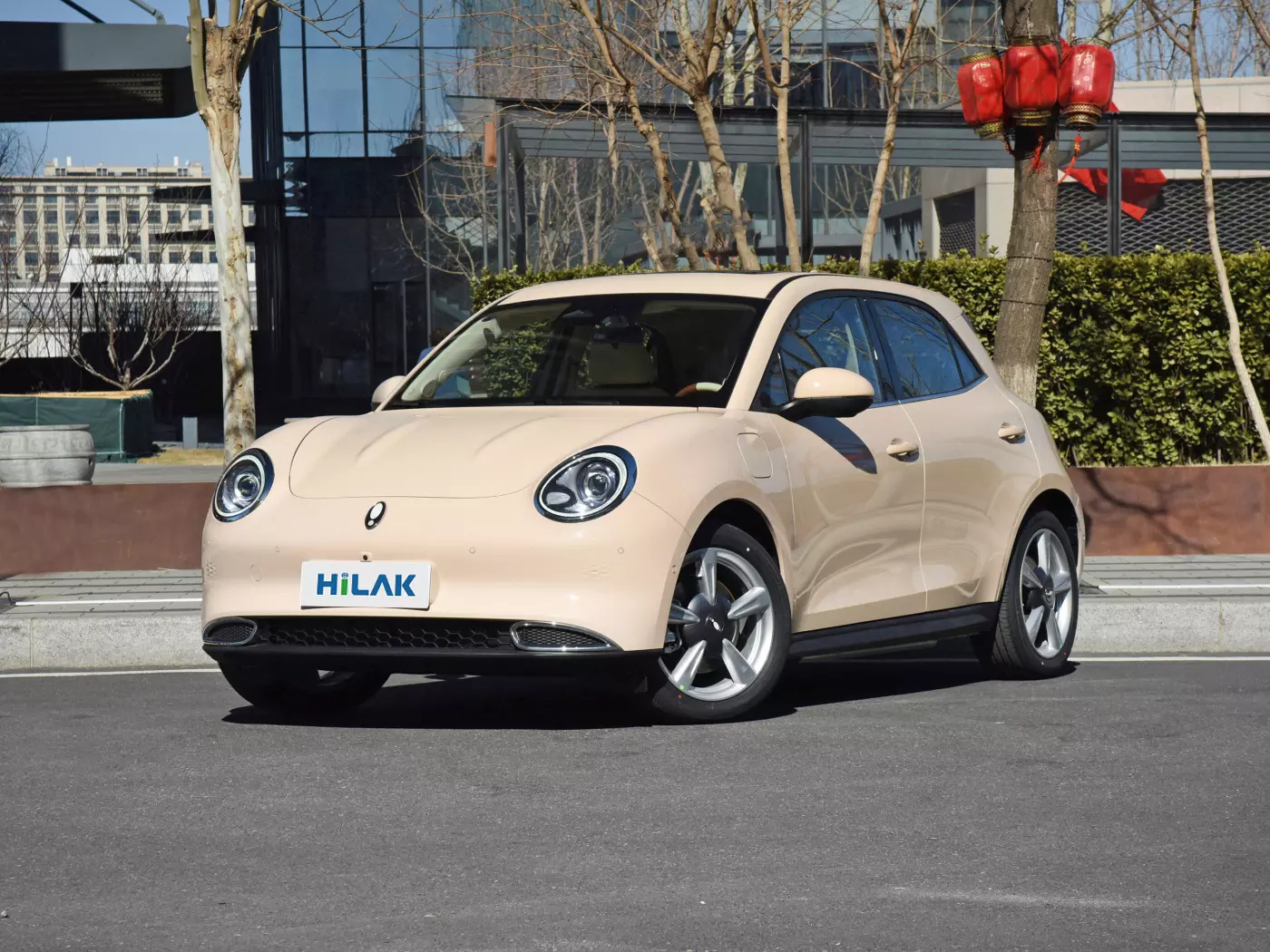 Close-up of the left front view of a cream-colored Ora Funky Cat electric car, with the vehicle parked on the side of the road on an asphalt road.