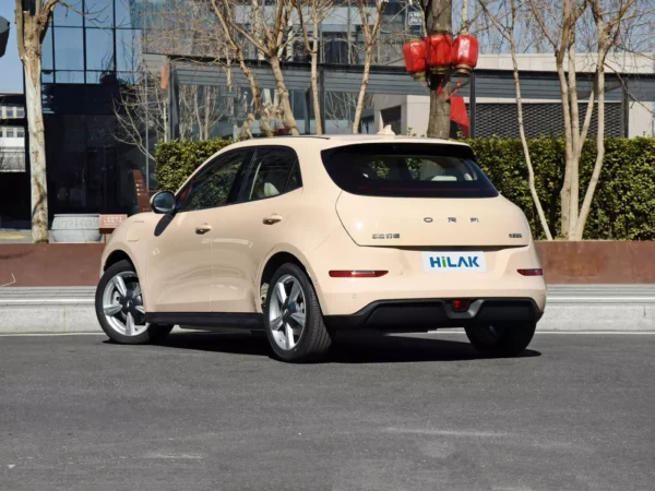 A close-up view of the left rear shot of a cream-colored Ora Funky Cat electric car, with the vehicle parked on the side of the road next to trees.