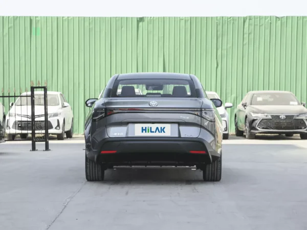 A front and rear view of a gray Toyota BZ3 with the vehicle on a concrete roadway with a green wall in the background.